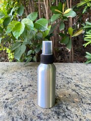 Spray Bottle by Green Bushes on Stone Surface