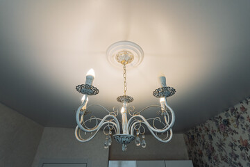 vintage chandelier casting warm light across ceiling, ornate glass arms and crystal details hang above floral wallpaper, soft ambient glow creates luxurious and cozy atmosphere in classic living space