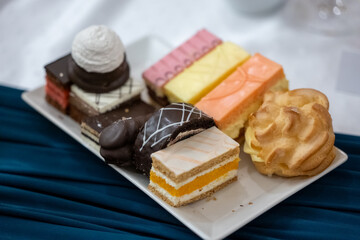 Assorted mini cakes and pastries on a white plate, including chocolate, cream, and fruit desserts, served at a celebration or event.