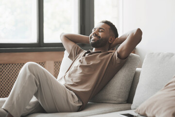 Satisfied handsome young man relaxing on sofa at home in living room, resting after a hard day...