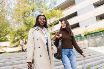 Fototapeta premium Two cheerful women walking down city steps, sharing a happy moment outdoors. Concept of friendship, diversity, and urban lifestyle
