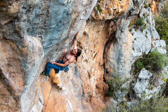 young athletic male climber with long hair climbs an overhanging rock. muscular young man. a man climbs a very difficult route. extreme sport, outdoor rock climbing