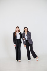 Two Asian women dressed in business attire posing on a clean white background, representing modern corporate roles, confident teamwork, and professional collaboration for office and company branding v
