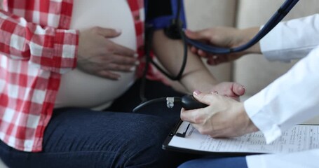 Physician measures blood pressure of pregnant woman at home. Doctor adjusts stethoscope against inner arm of female and checks blood pressure monitor - Powered by Adobe