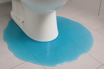 Problematic toilet leak with blue water damage on bathroom floor. This messy plumbing problem requires immediate repair