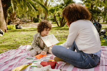 Son and his mother look at a drawing in a sketchbook she is holding while sitting on a blanket