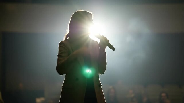 Woman speaker with microphone delivering presentation on stage, communicating ideas to audience during conference or seminar.