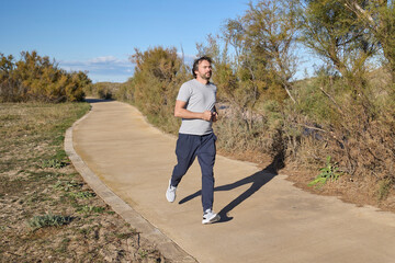 Man jogging along paved path surrounded by nature.