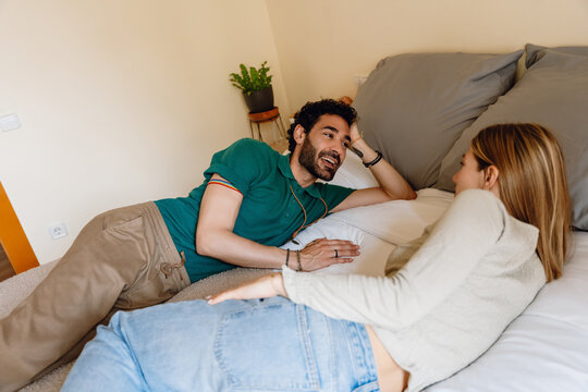 A man smiles and talks to a woman lying next to him on the bed