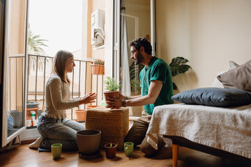 A man holds a potted plant while talking to a woman sitting across from him