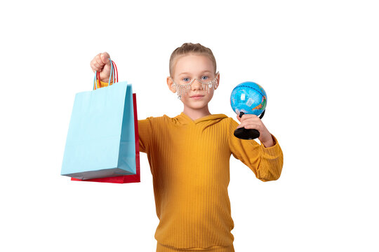 Smiling girl in yellow sweater holding colorful shopping bags and a globe, standing against a transparent background. Concept of global shopping and childhood curiosity.