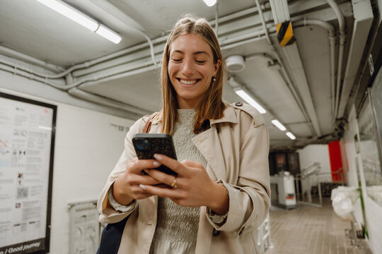 Woman typing on phone while walking down hallway and smiling