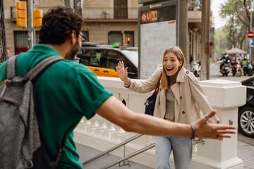 A woman laughs and waves as she approaches a man who is holding his hand out to the side