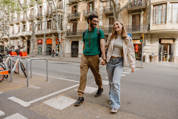 Obraz premium A man and a woman laugh and hold hands while crossing the road