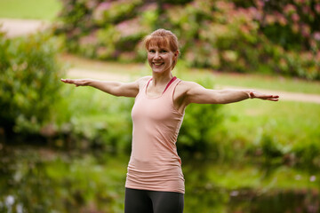 Woman, yoga and smile in portrait at park with stretching arms, confident or outdoor by stream in summer. Person, happy and holistic fitness in nature, flexibility or wellness by river in New Zealand