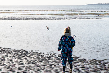 Fillette en combinaison et bottes face à la mer et aux mouettes