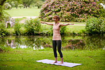 Woman, yoga and smile at park with stretching arms, mindfulness or outdoor by stream in summer. Person, happy and holistic fitness in nature, self care or breathe for wellness by river in New Zealand