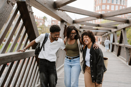 A group of three friends hugging and laughing while walking on a bridge