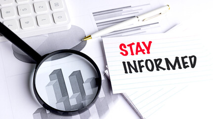 Stay informed message on lined card with magnifying glass, charts, pen and calculator on desk