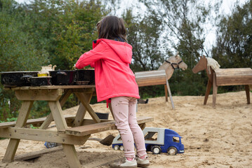 Rear view of a little girl playing a mud kitchen game on a picnic table.
