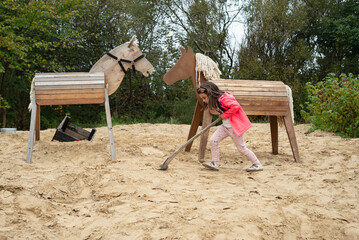 5-year-old girl digging with a shovel in a big sandbox.