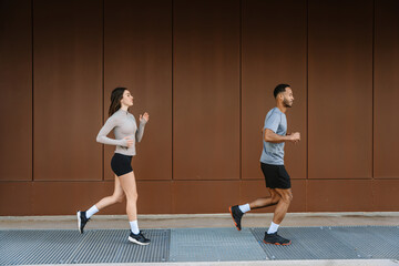 A male athlete runs while a female athlete runs behind him