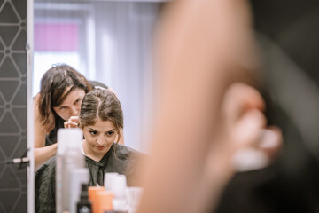 Young woman with long hair is having her hairstyle done by a stylist in a modern salon, surrounded by beauty products and mirrors, showcasing a hairdressing experience