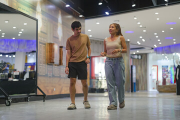 A young couple walking through the brightly lit, modern hallway of a shopping mall.