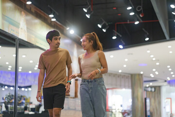 A young couple walking through the brightly lit, modern hallway of a shopping mall.