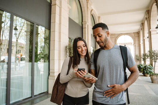 Female athlete laughing and listening to male athlete talking while they stand and look at their phones showing - Powered by Adobe