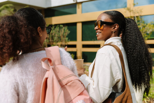 A female student holds a cup and smiles while listening to a female student walking next to her