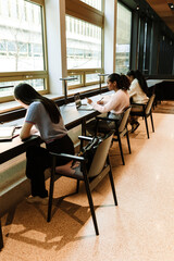Obraz premium A group of three female students sit on chairs at a table while one of them looks at a laptop and holds a pen over a notebook
