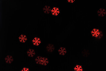 Red glowing snowflake shapes against a dark background create a festive abstract bokeh scene with soft vibrant light.