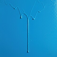 Vibrant blue paint drips slowly down a freshly coated surface, indicating it is still wet and should not be touched. A caution for new finishes ,warning ,material ,liquid