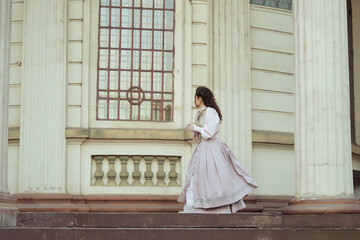 Fototapeta premium An elegant woman in a vintage dress stands by an old stone column
