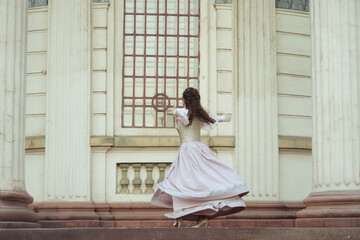 Fototapeta premium An elegant woman in a vintage dress stands by an old stone column