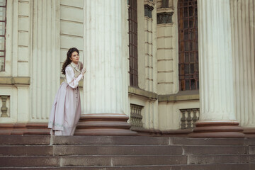 Fototapeta premium An elegant woman in a vintage dress stands by an old stone column