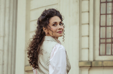 Fototapeta premium An elegant woman in a vintage dress stands by an old stone column