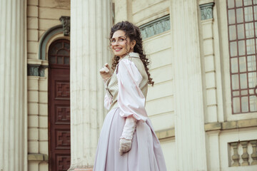 Fototapeta premium An elegant woman in a vintage dress stands by an old stone column