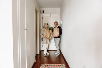 Man gesturing and talking to woman who is laughing while they are holding packages and standing
