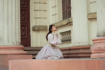 Fototapeta premium An elegant woman in a vintage dress stands by an old stone column