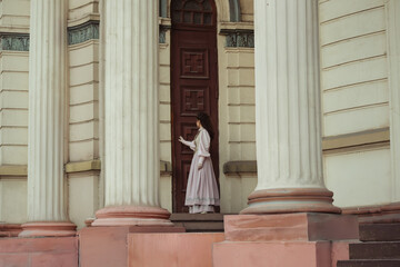 Fototapeta premium An elegant woman in a vintage dress stands by an old stone column
