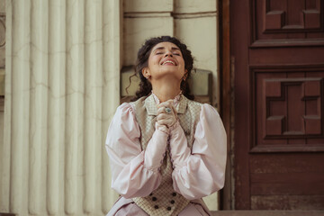Fototapeta premium An elegant woman in a vintage dress sits next to an old stone column with a very happy expression on her face.