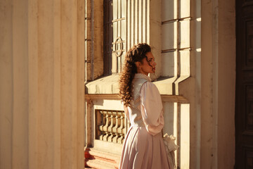 Fototapeta premium An elegant woman in a vintage dress stands by an old stone column