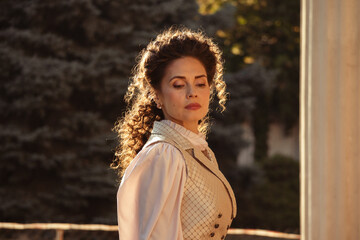 Fototapeta premium Portrait of a woman in vintage clothing, illuminated by warm sunlight, against a backdrop of ancient architecture.