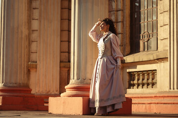 Fototapeta premium An elegant woman in a vintage dress stands by an old stone column