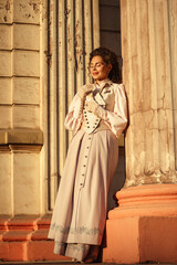 Fototapeta premium An elegant woman in a vintage dress stands by an old stone column