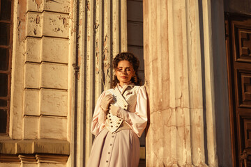 Fototapeta premium An elegant woman in a vintage dress stands by an old stone column