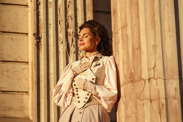 Fototapeta premium An elegant woman in a vintage dress stands by an old stone column
