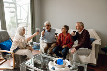 Group of four friends talking and holding glasses while sitting on a chair and sofa while one of them is about to drink